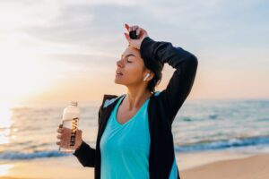 A woman wiping her forehead in the heat while holding a bottle of water
