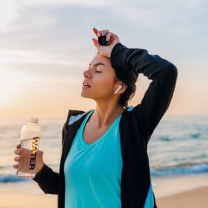 A woman wiping her forehead in the heat while holding a bottle of water