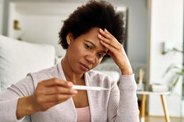Black woman feeling worried while measuring her temperature at home.